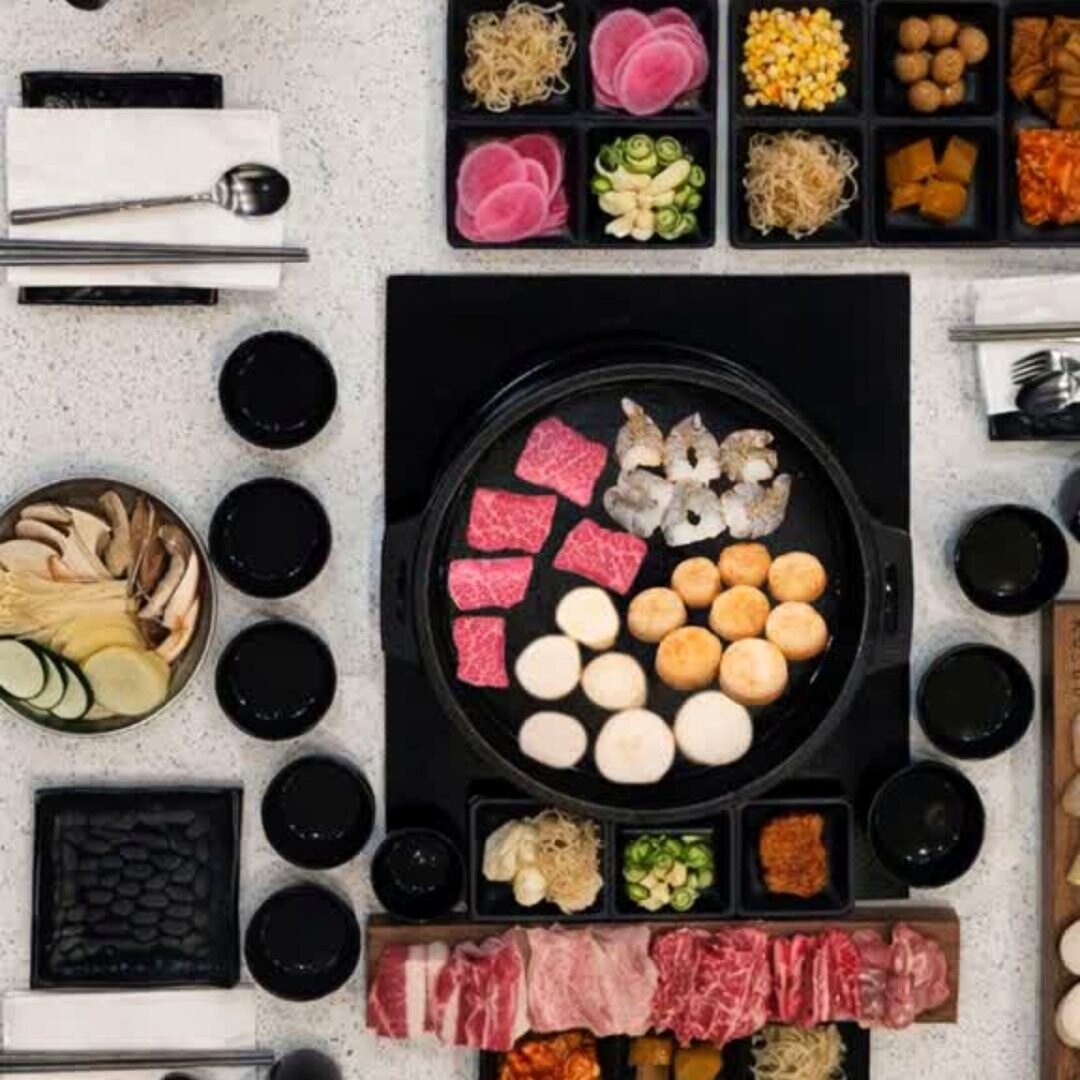 KOSOO all-you-can-eat table from above — grill with beef, prawns and scallops, surrounded by banchan