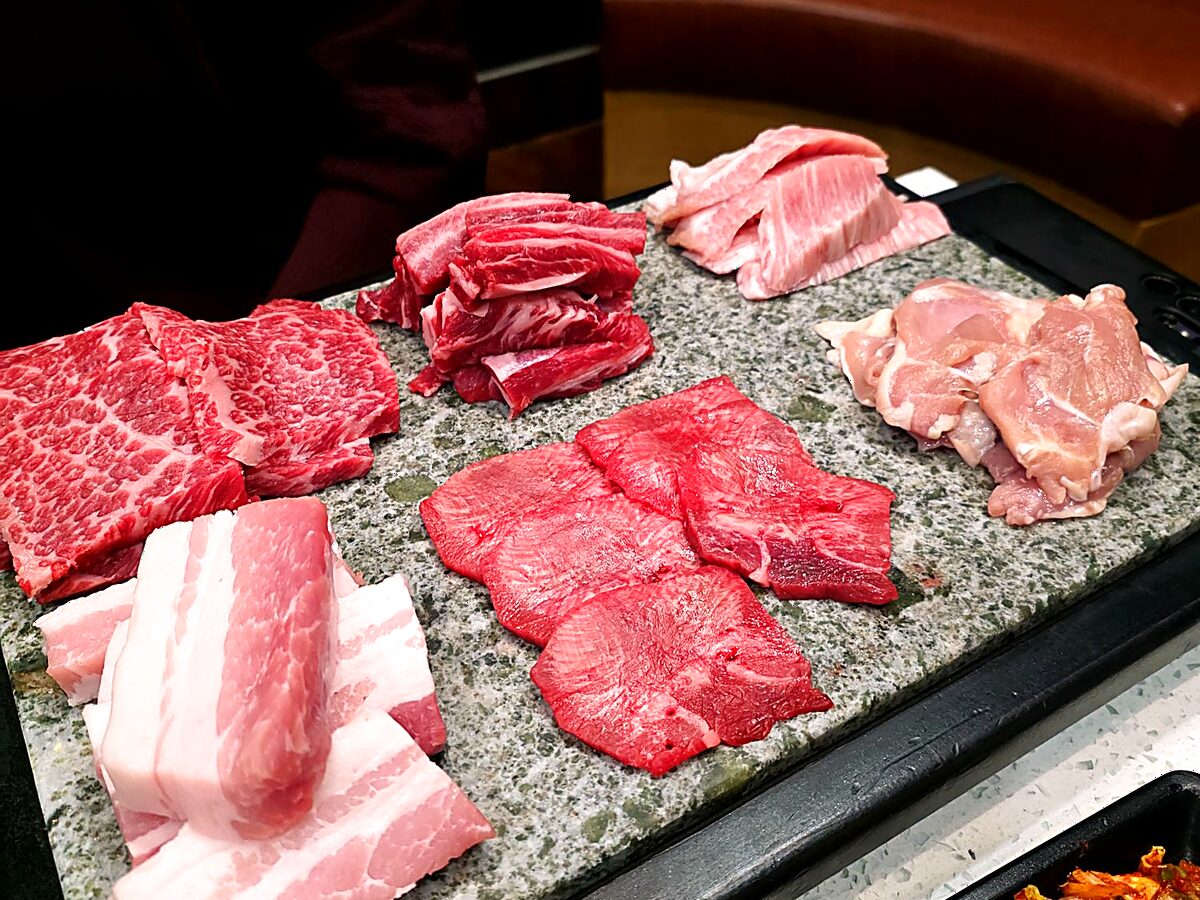 Premium raw meats on a stone platter — beef, pork belly and chicken for the grill
