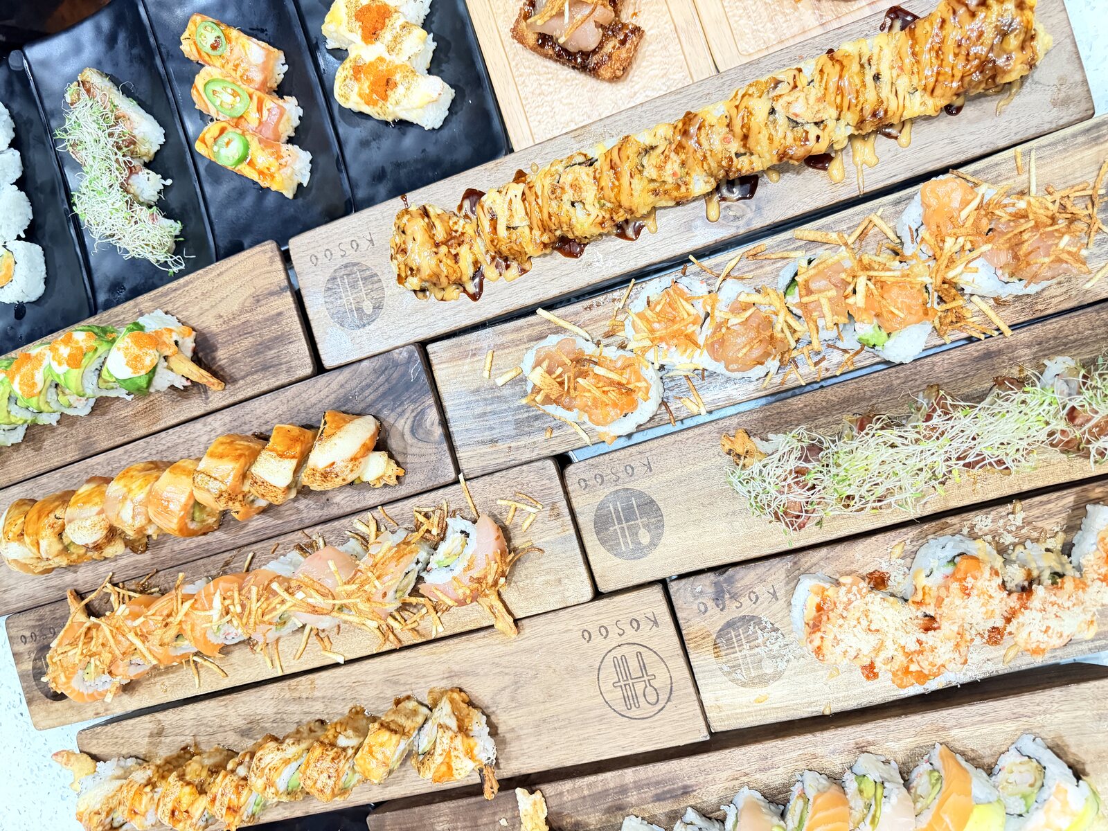 KOSOO sushi spread — rolls, oshi and crispy rolls on wooden boards, now included in all-you-can-eat